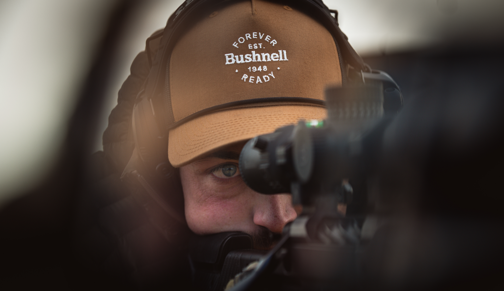 Man looking through a scope in a hat
