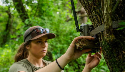 woman setting up trail camera in the forest