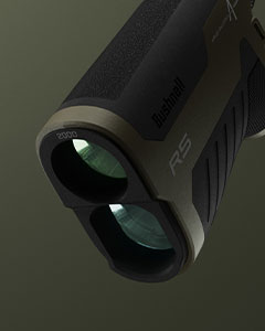 Close-up view of the lens end of a Bushnell R5 rangefinder, showing two circular lenses with a dark, textured body against a greenish background.