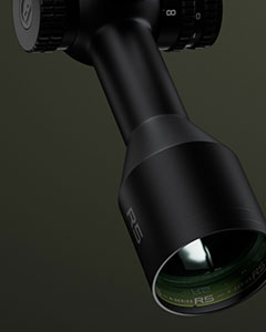 Close-up of a black optical scope or rifle scope with “RS” marked on the lens housing, set against a dark green background.