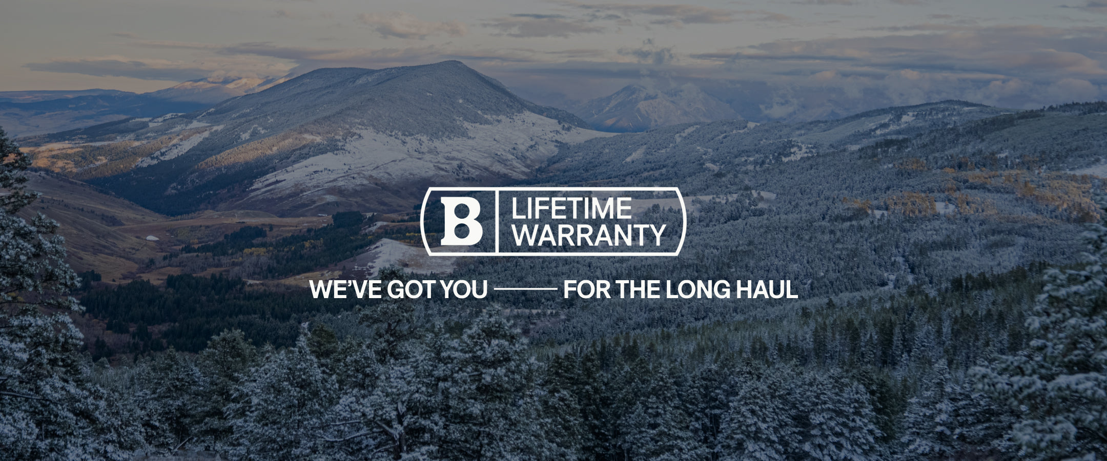 Snowy mountains and forests under a cloudy sky, with the text “B Lifetime Warranty” and “Weve got you — for the long haul” displayed prominently in the center.