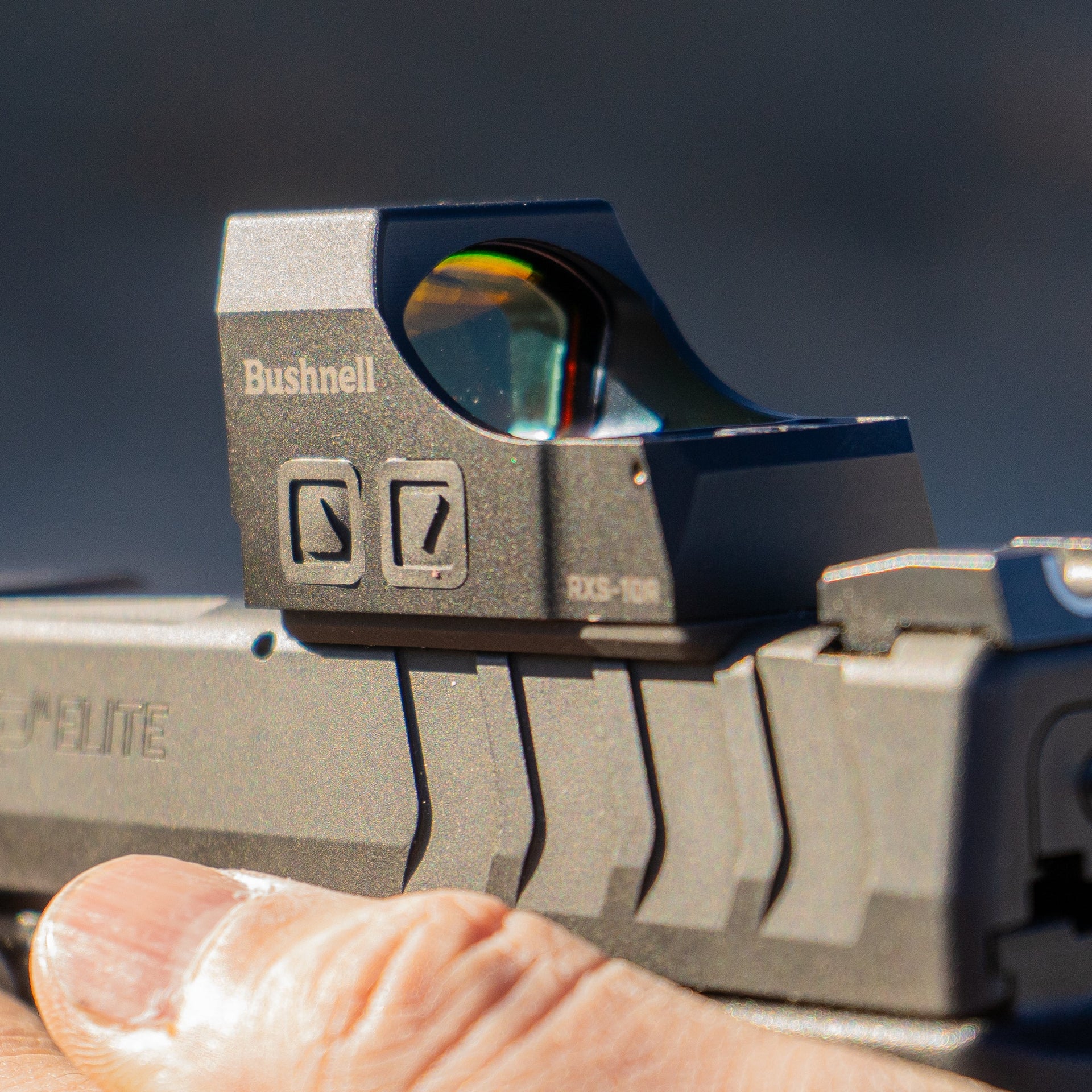 Hand holding a gun with a red dot sight against a blurred background