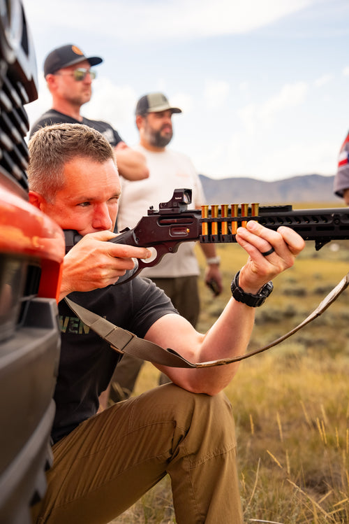 Man holding a rifle in a field with mountains in the background