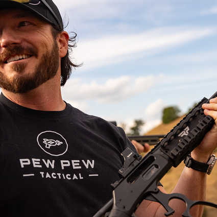 Man holding a rifle with 'Pew Pew Tactical' shirt outdoors