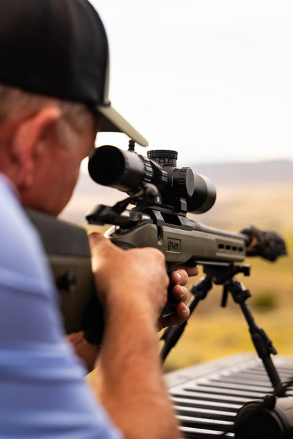 Person aiming a rifle with a scope in a natural setting
