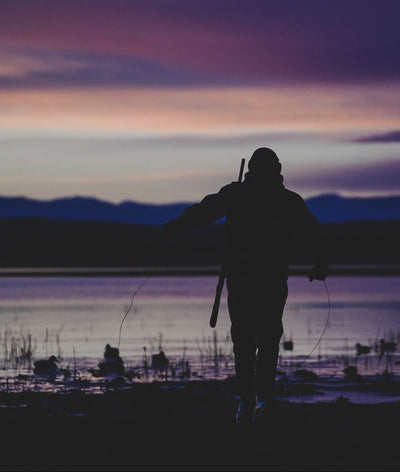 Silhouette of a person walking along a lake at sunset with mountains in the background