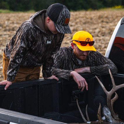Two hunters in camouflage clothing with a deer in the back of a pickup truck.
