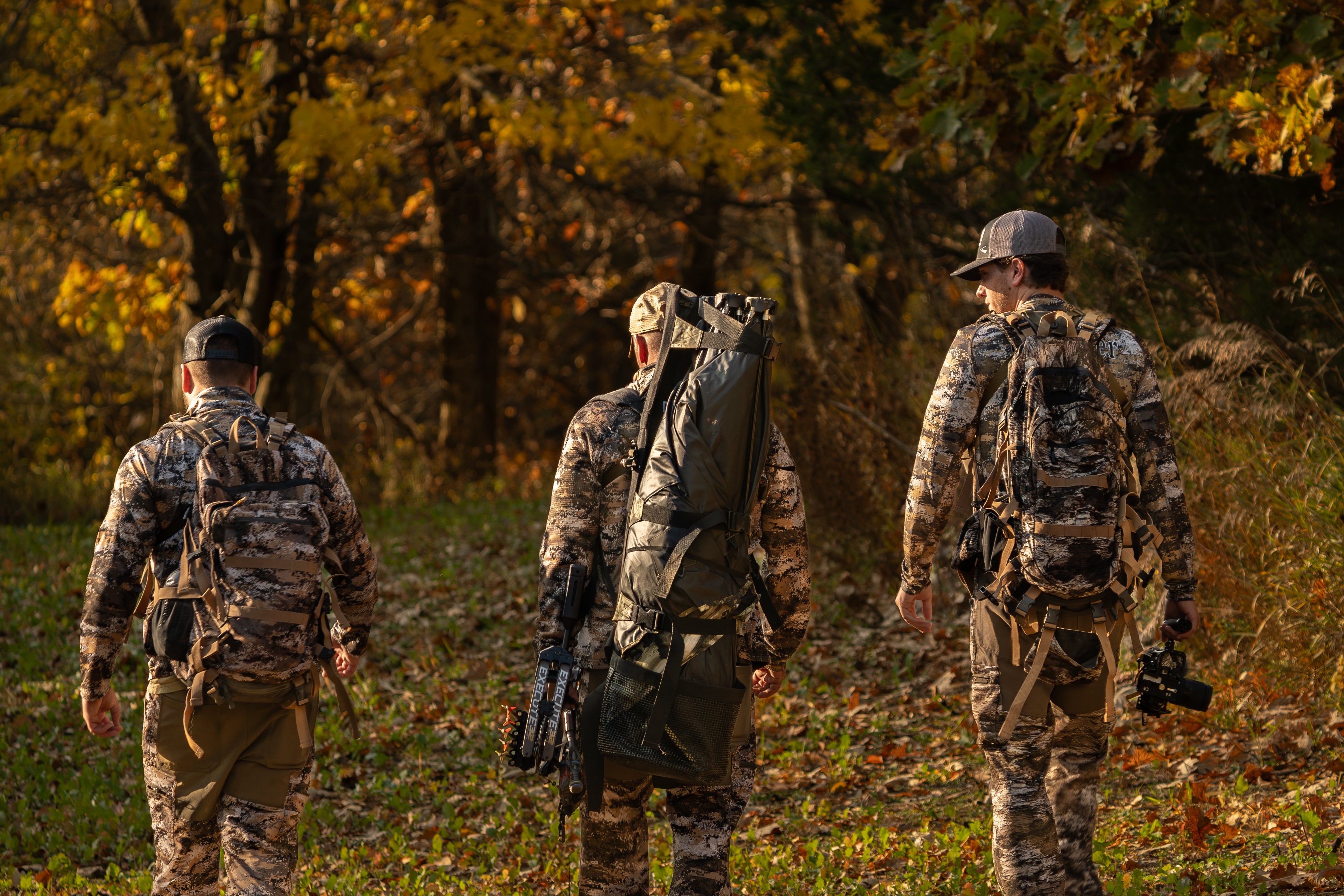 Three hunters in camouflage walking through a forest during autumn.