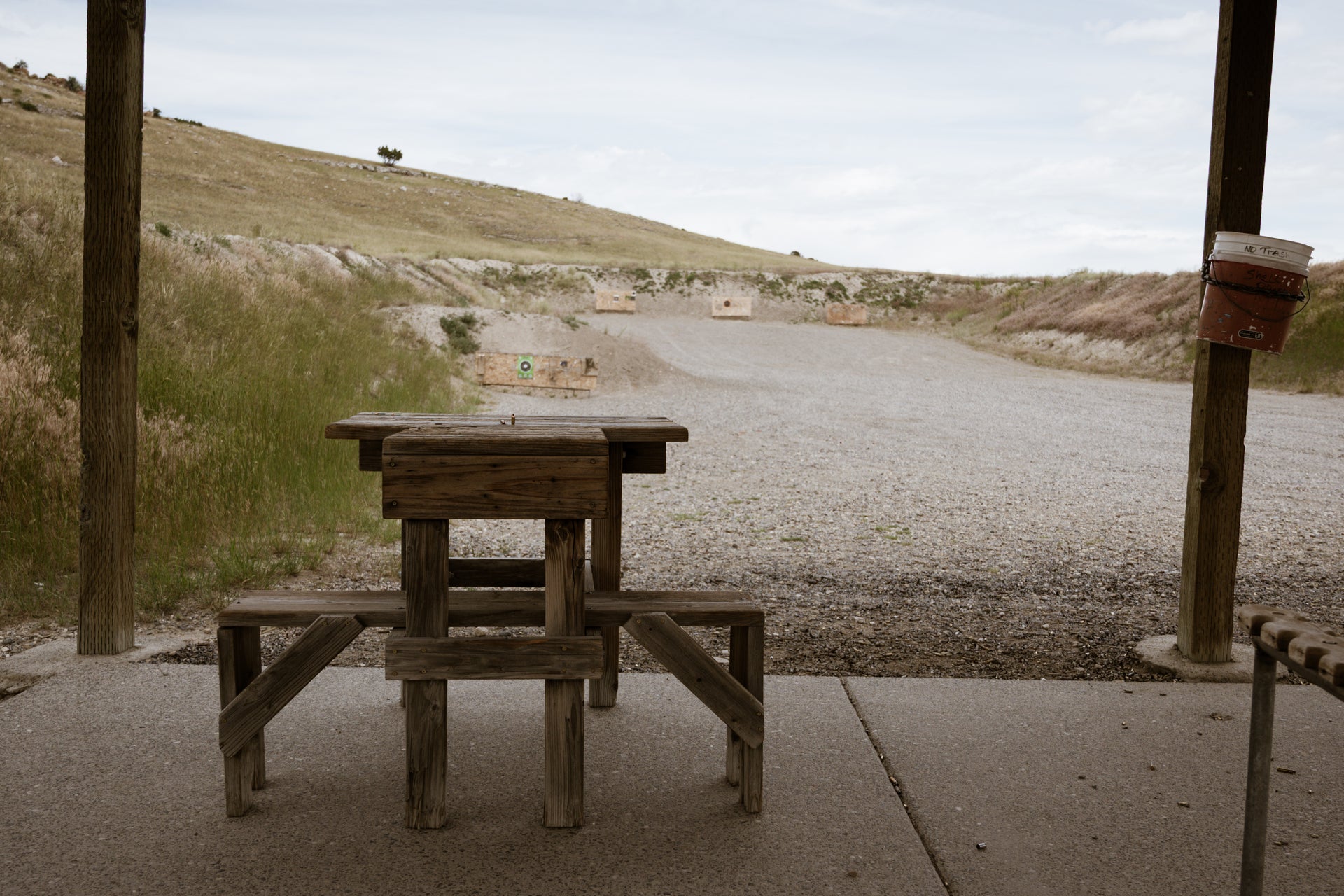 Wooden picnic table on a gravel road with a grassy hill in the background