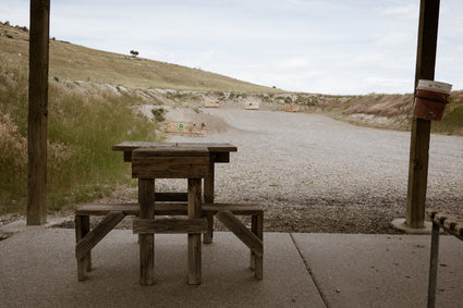 Wooden picnic table on a gravel road with a grassy hill in the background