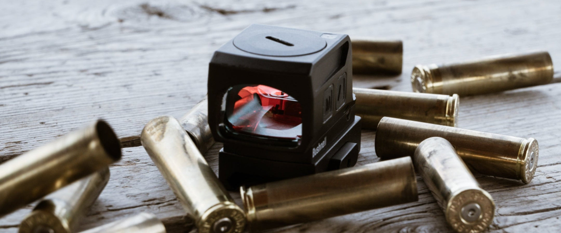 Small black device with a red light surrounded by gold bullets on a wooden surface