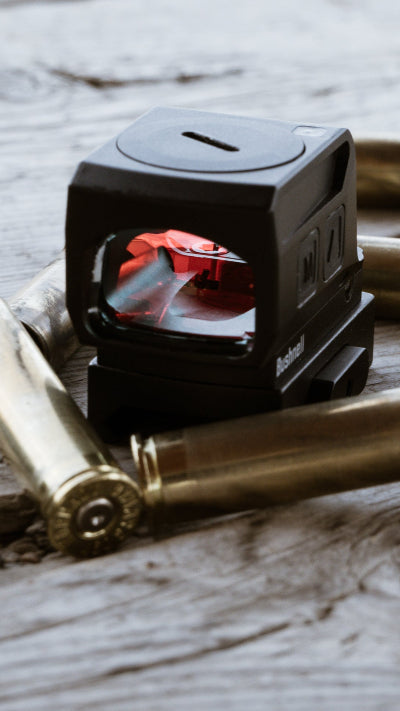 Small black device with a red light surrounded by gold bullets on a wooden surface
