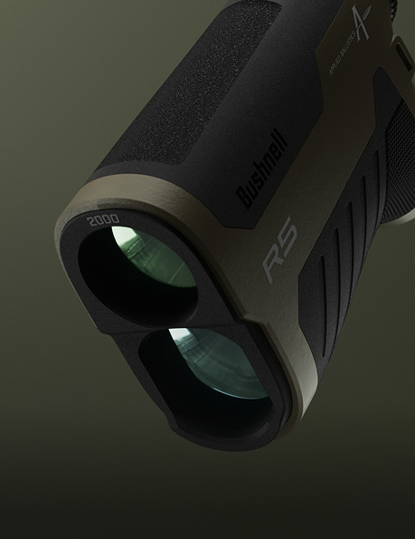 Close-up view of a Bushnell R5 rangefinder, showing its dual lenses and textured black and tan exterior against a dark background.