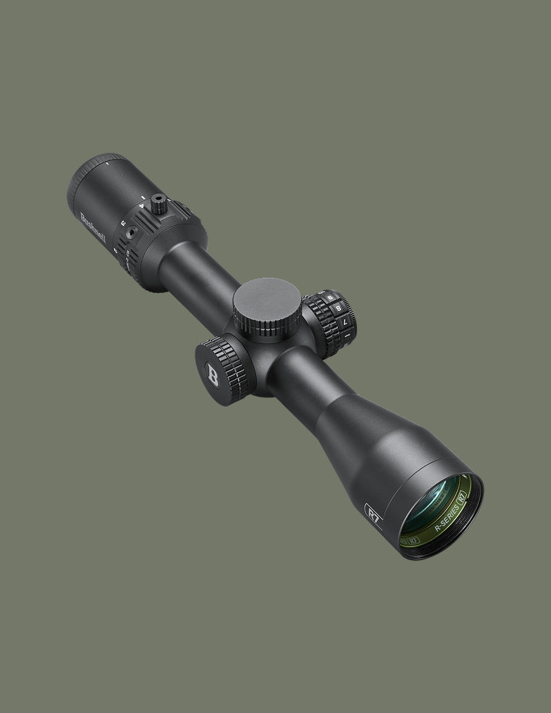 A black tactical rifle scope photographed at an angle against a solid dark olive green background.