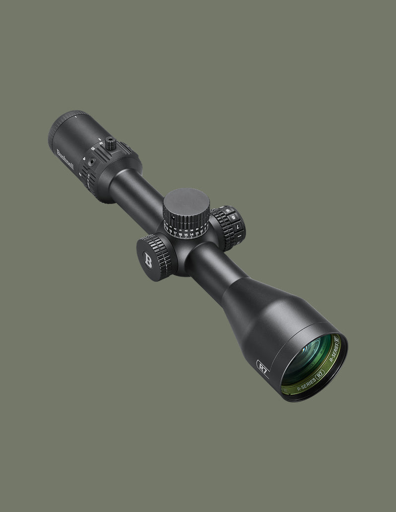 A black rifle scope with textured adjustment knobs and a green-tinted lens, shown at an angle against a solid dark olive green background.