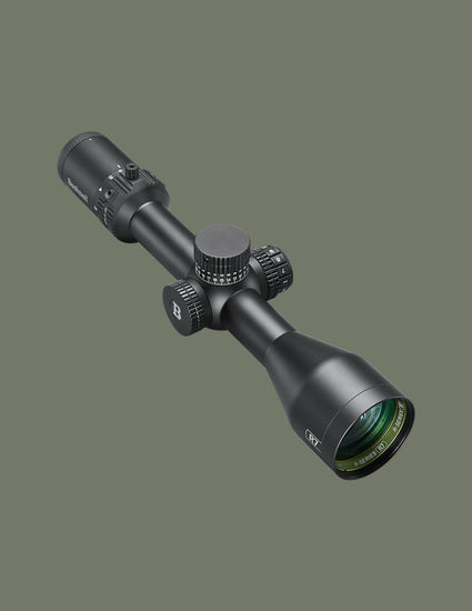 A black rifle scope with textured adjustment knobs and a green-tinted lens, shown at an angle against a solid dark olive green background.