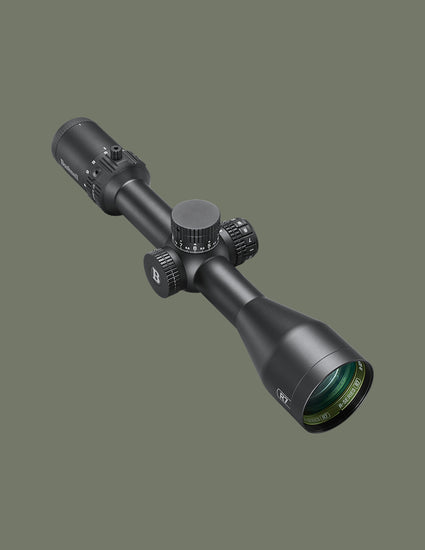 A black tactical rifle scope with adjustment knobs and a green-coated objective lens, shown at an angle against a solid dark olive-gray background.