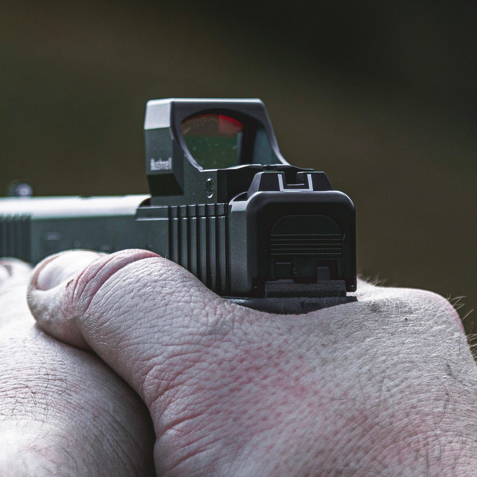 Hand holding a rifle with a red dot sight against a blurred background
