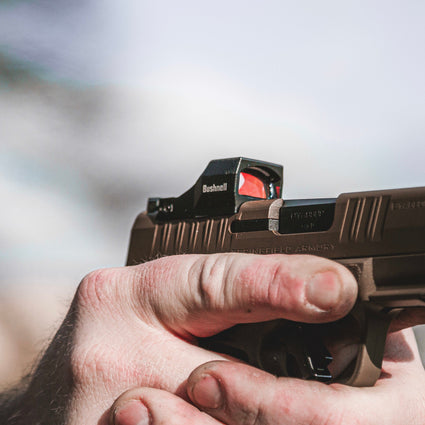 Hand holding a handgun with a blurred outdoor background