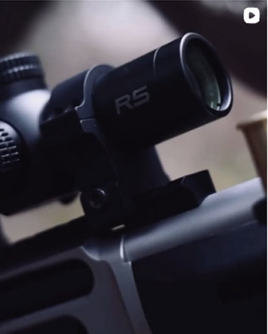 Close-up of a rifle scope with 'R5' branding on a blurred background