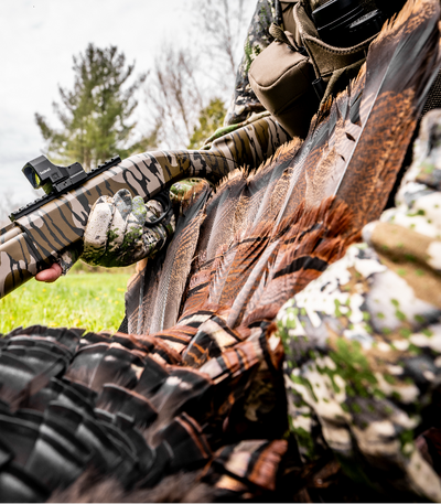 Hunter in camouflage holding a rifle with a scope, outdoors.