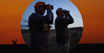 Two hunters using binoculars with a sunset or sunrise background