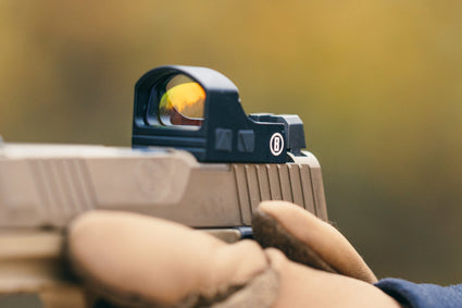 Hand holding a handgun with a sight against a blurred natural background