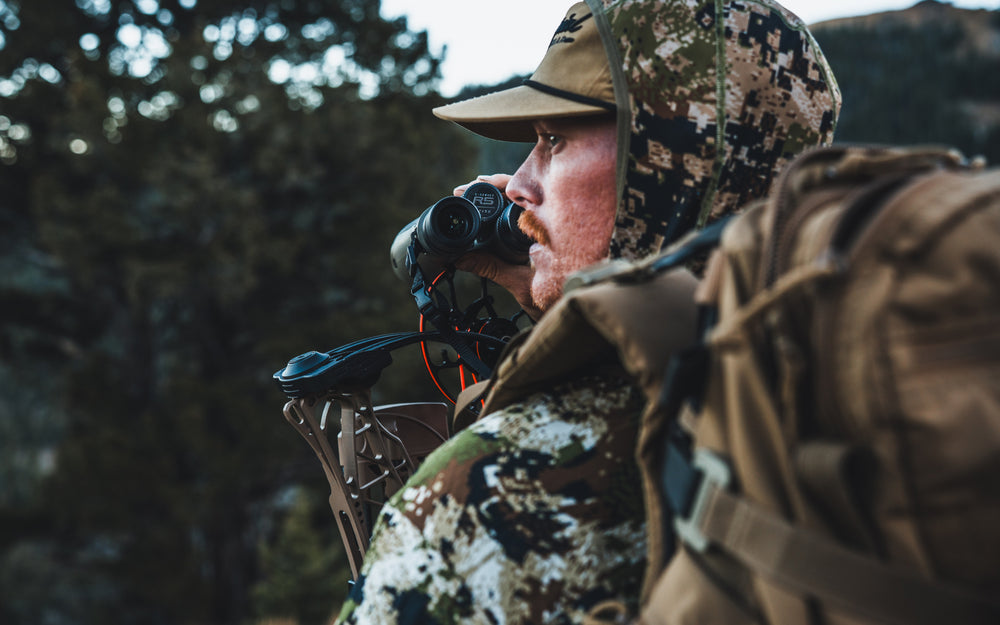 Hunter in camouflage gear using binoculars in a forest setting