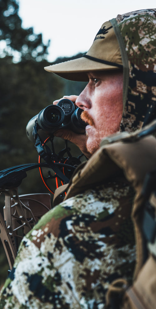 Man in camouflage gear using a binoculars in a forest setting