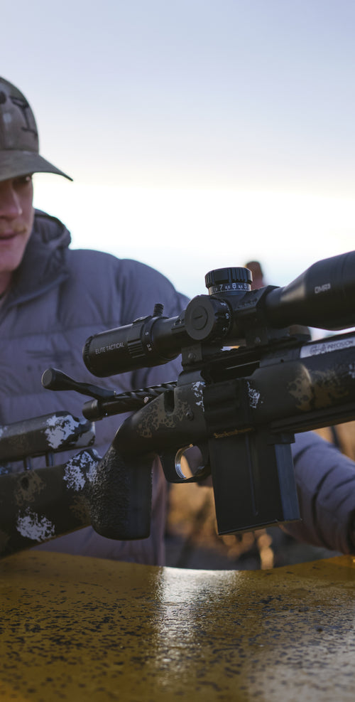 Person holding a rifle with a scope, blurred background