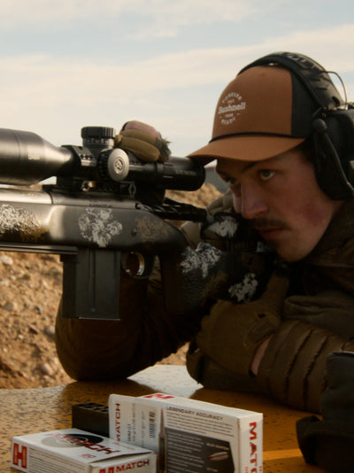 Person aiming a rifle with a scope in a natural setting