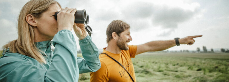 Couple in an open grassy birding with a pair of binoculars
