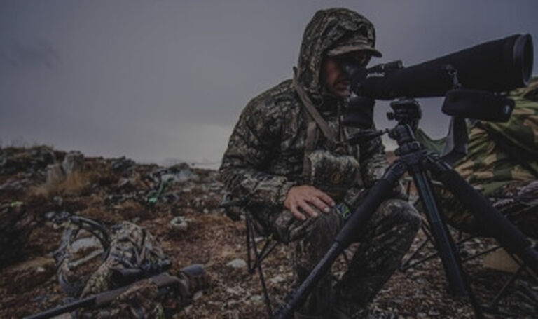 Man in camouflage on rocky terrain looking through Spotting Scope