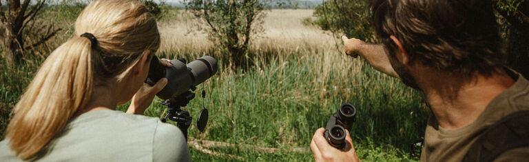 Man and woman in grassy filed using Bushnell Spotting Scope and Binoculars