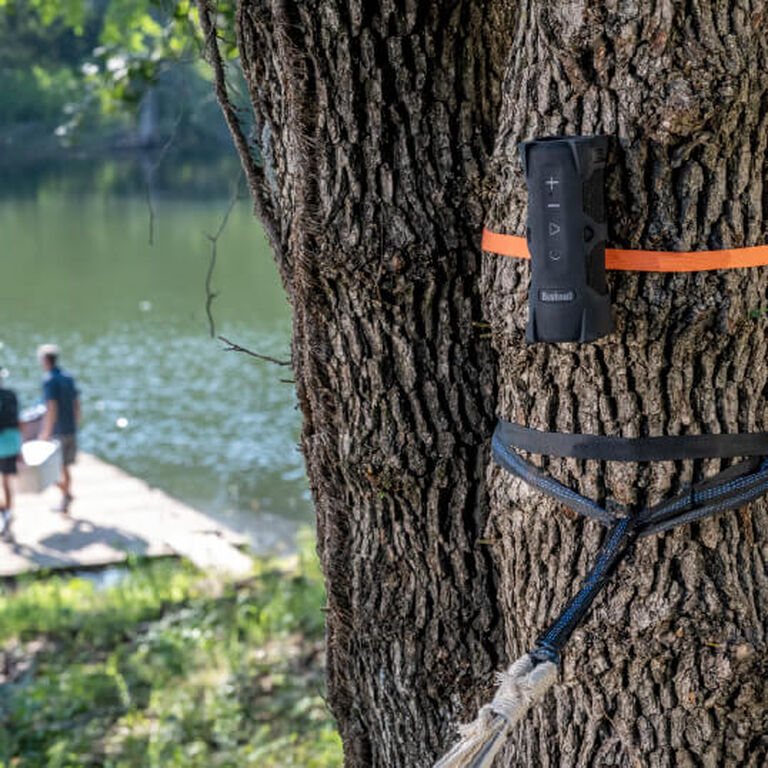 Outdoorsman Bluetooth Speaker strapped to a tree at a lake