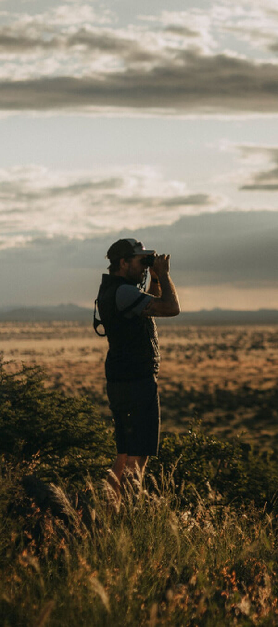 Man in grassy field looking through Bushnell Binoculars