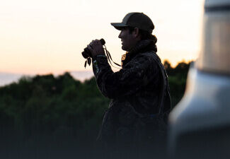 Man standing in a field holding binoculars in low light