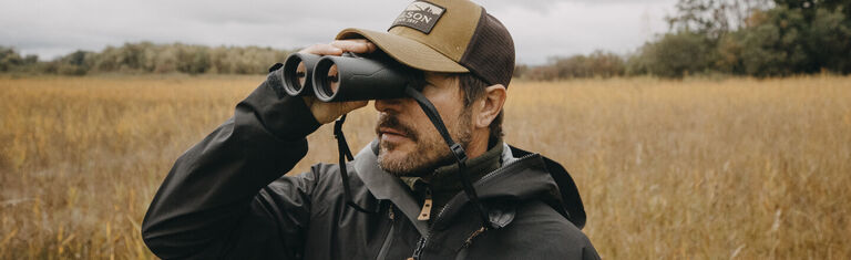 Man in grassy field looking through Bushnell Binoculars